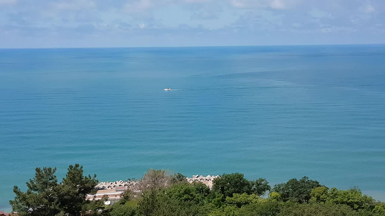 在一个阳光明媚的夏日，一艘小船在碧绿平静的海面上航行的航拍照片视频下载