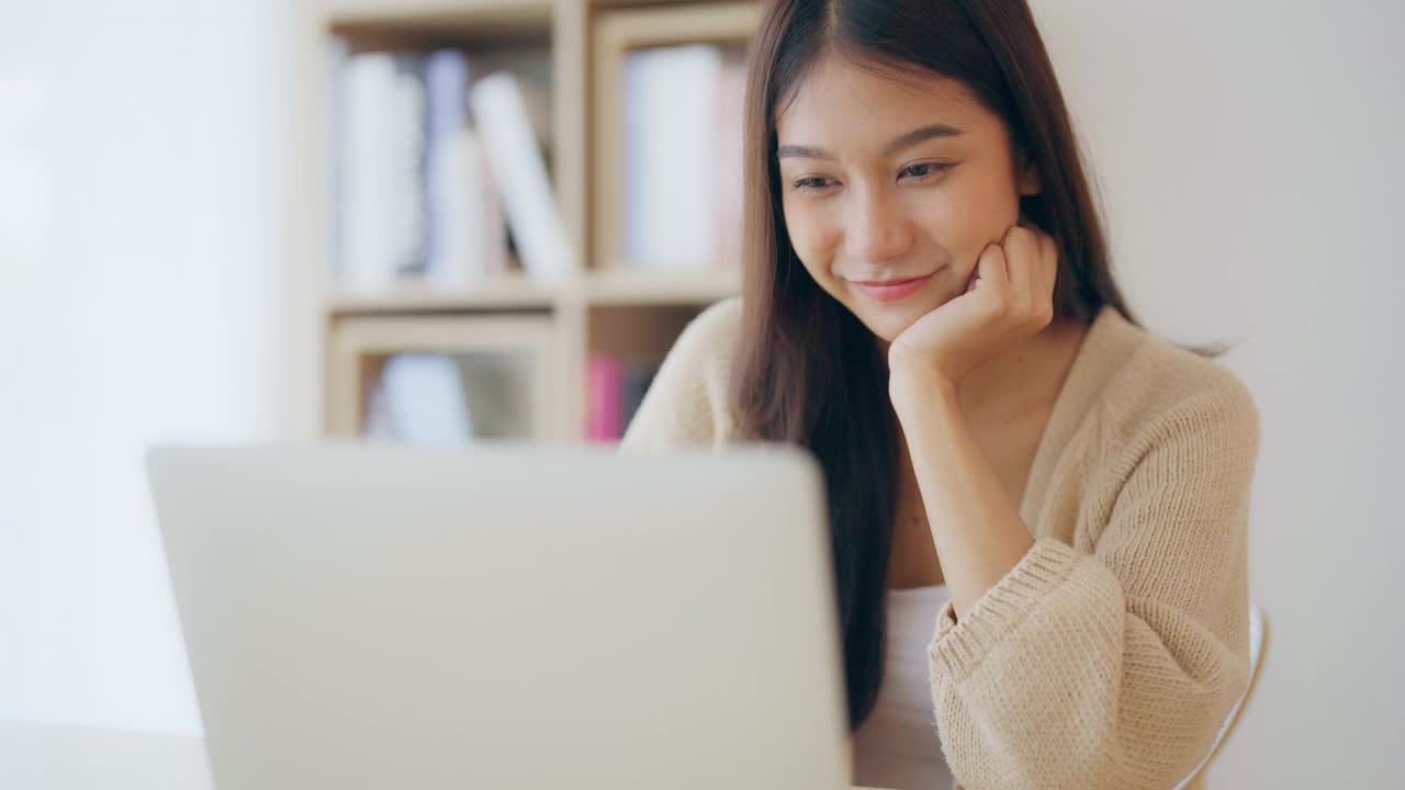 年轻的亚洲女性在家工作。快乐的女性在家里的桌子上使用笔记本电脑视频素材