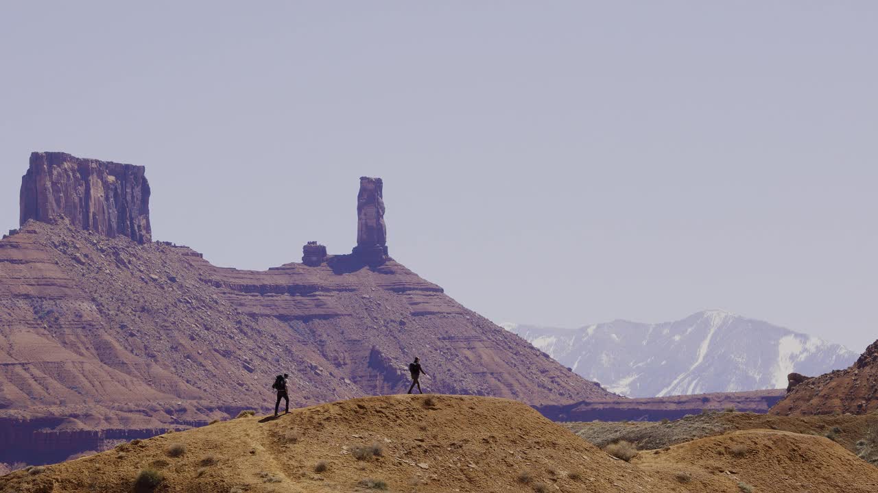 徒步旅行者走在Moab犹他州的沙漠岩层支柱和雪山的背景男人和女人一起宽帧复制空间视频素材