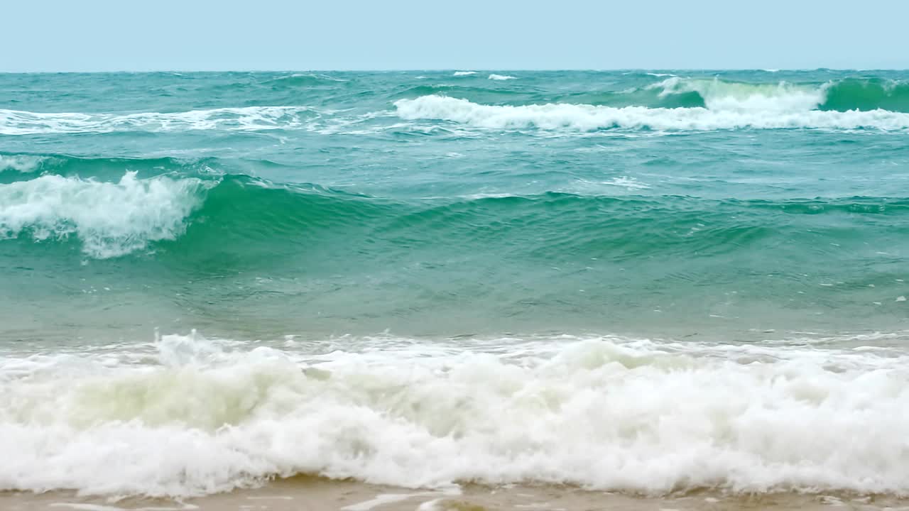 海浪在多云的天空背景，地平线上的场景，美丽的海滩与破碎的海浪，中景，慢动作，高清。ProRes 422 HQ。视频素材