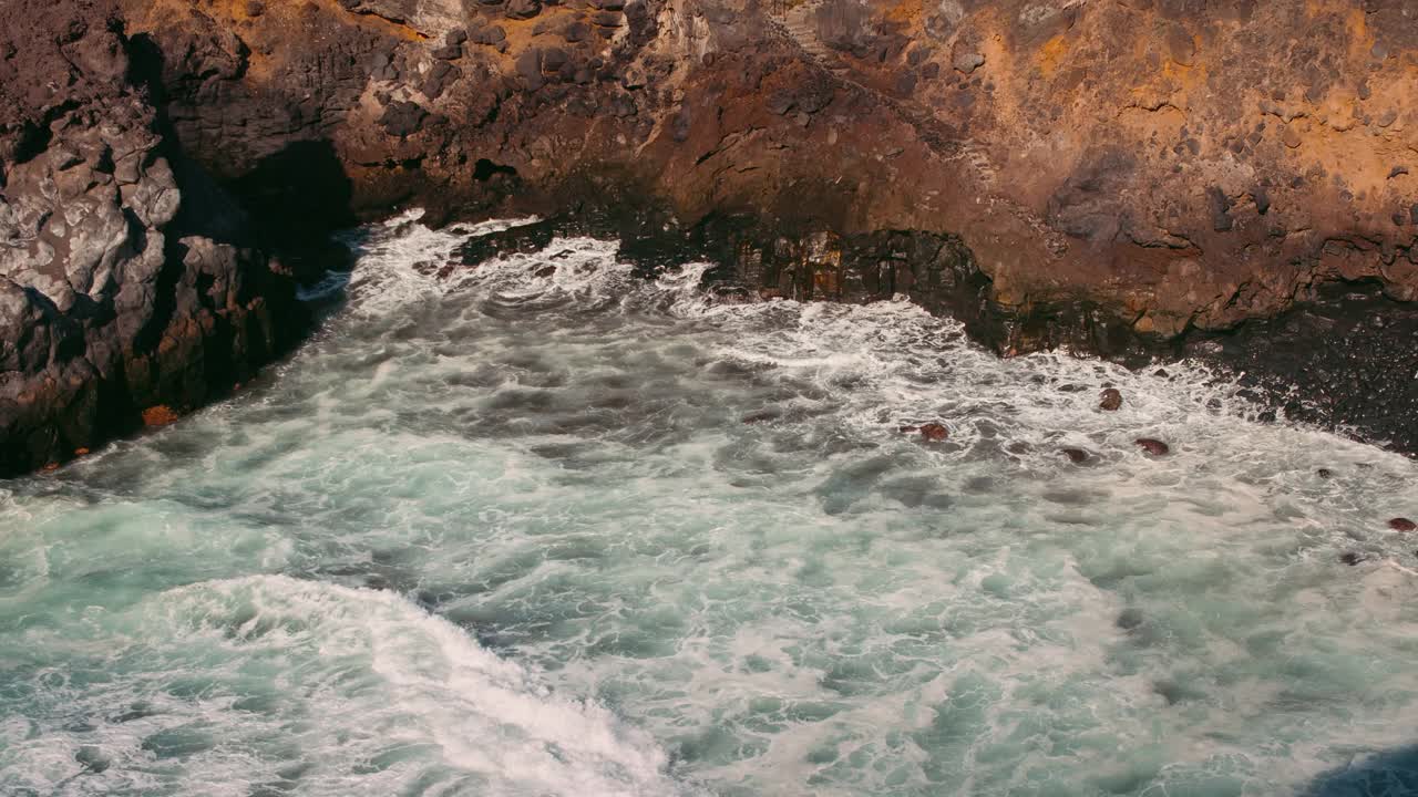 巨大的海浪冲击着岩石悬崖，溅起白色的泡沫。特写慢镜头汹涌的河水。视频素材