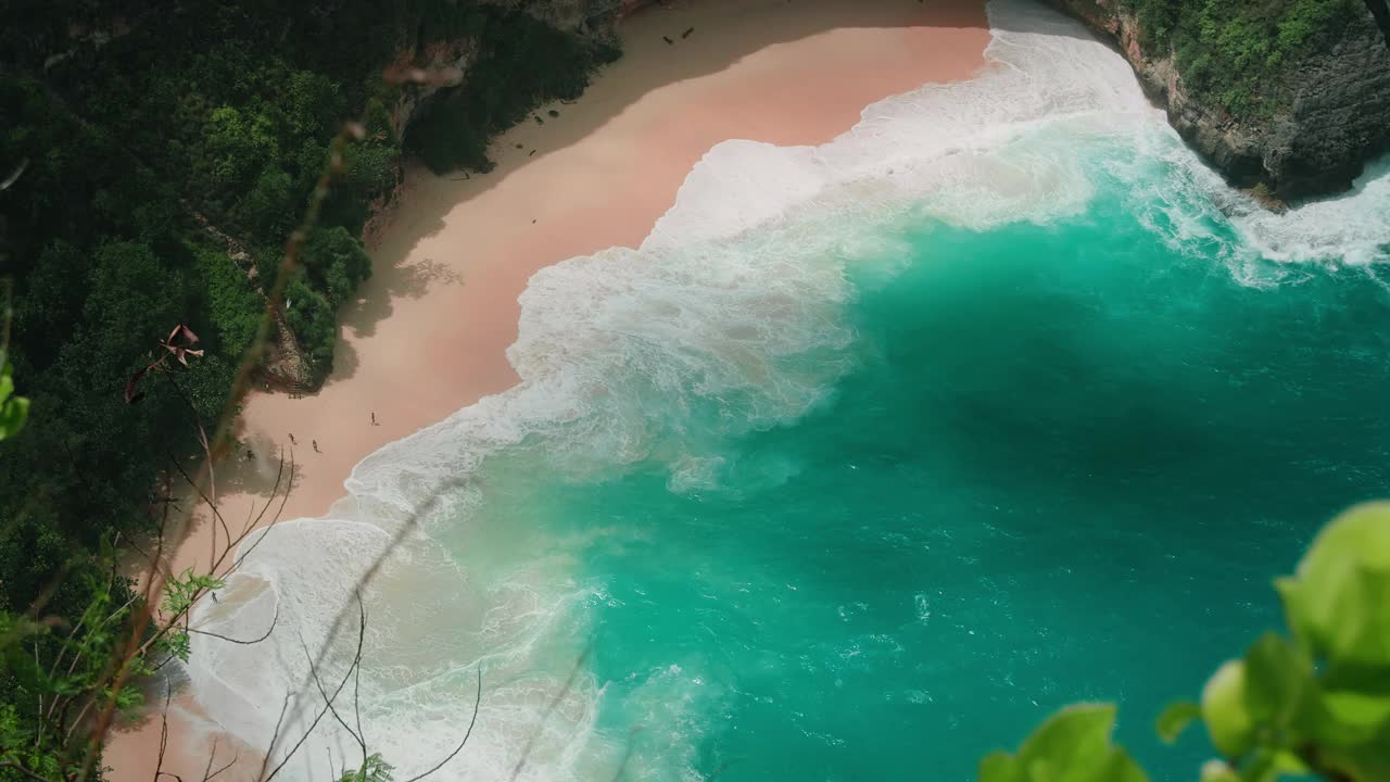 热带海滩，光滑的粉色沙滩和迷人的蔚蓝海浪。俯瞰美丽的海景，海岸线上有绿色的棕榈树森林。视频素材