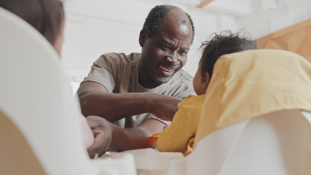 快乐的黑人爸爸在高脚椅上喂两个婴儿视频素材