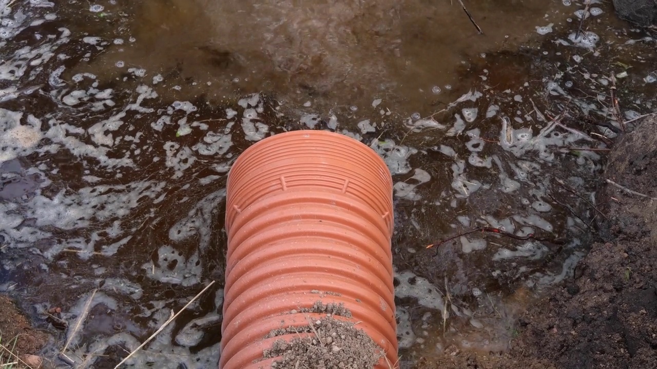 排水管内有水流流动。雨水管理在公共空间，塑料管，岩石和灌木种植。污水系统的塑料管。地下管道系统。视频素材