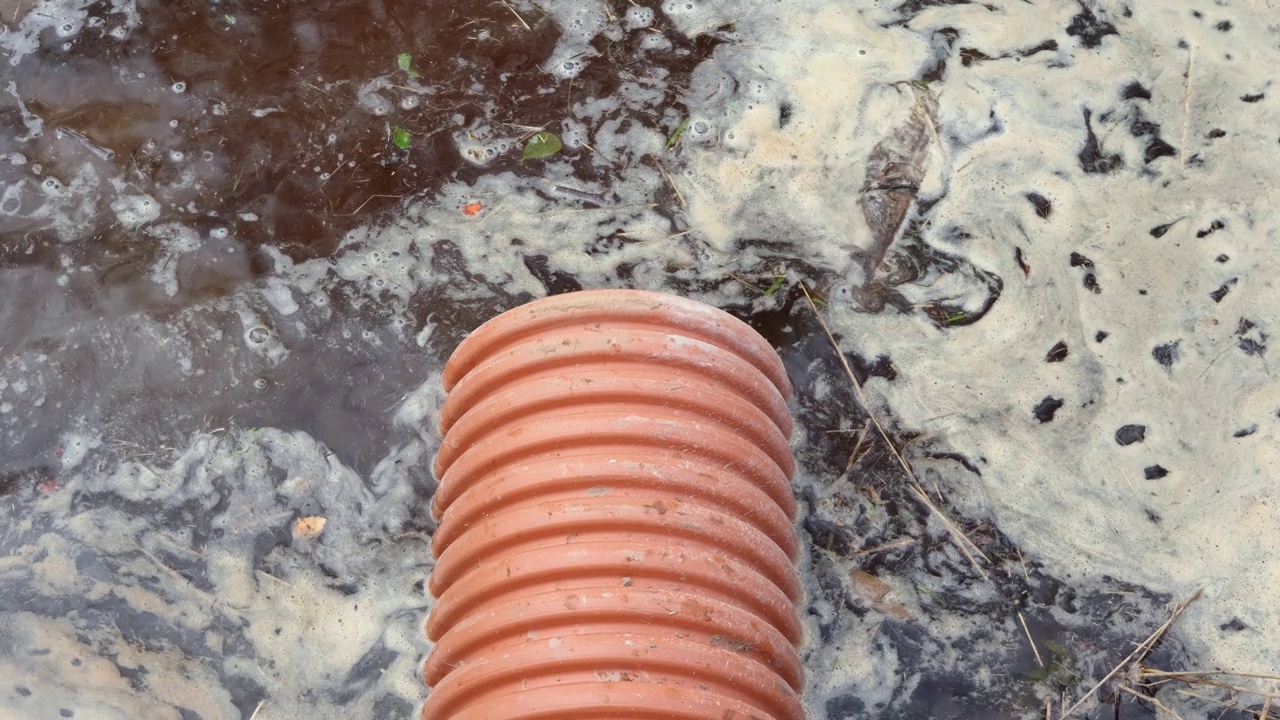 排水管内有水流流动。雨水管理在公共空间，塑料管，岩石和灌木种植。污水系统的塑料管。地下管道系统。视频素材