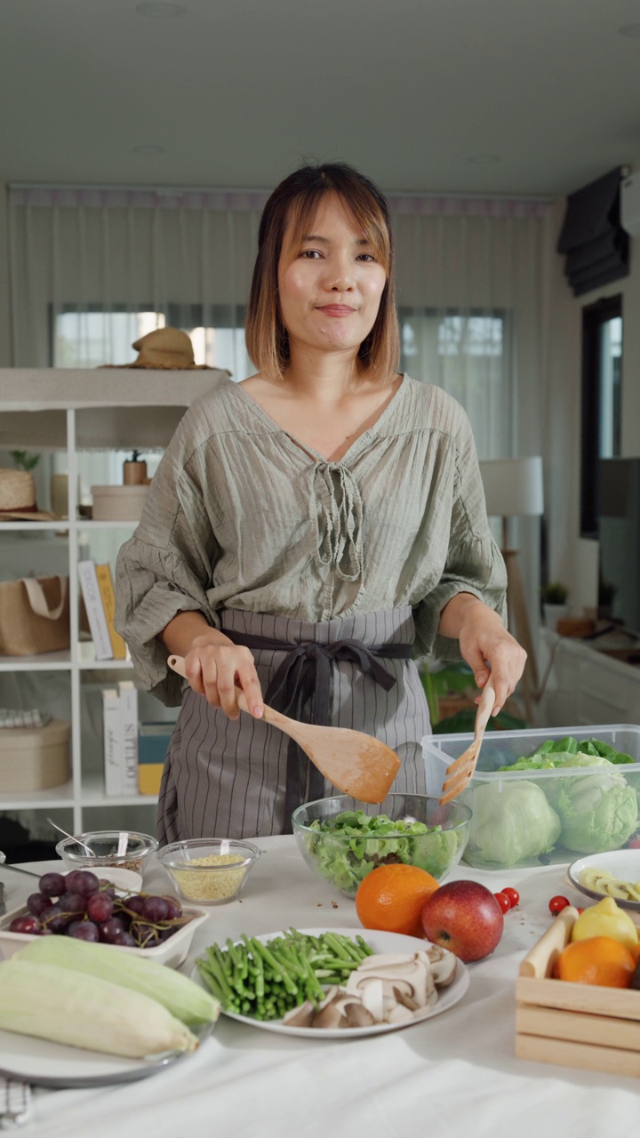 年轻的亚洲女性博主在线影响者录制视频内容在家里的餐桌上烹饪沙拉。生活方式健康饮食享受生活和植物性饮食。垂直的屏幕。视频素材