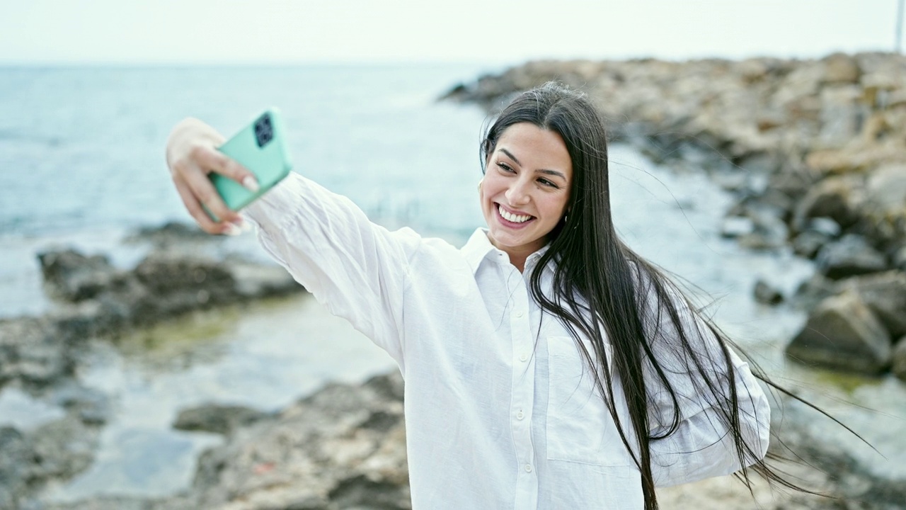 年轻美丽的西班牙女子在海边用智能手机自拍视频素材