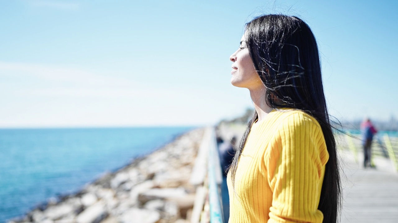 年轻美丽的西班牙女人闭着眼睛在海边呼吸视频素材