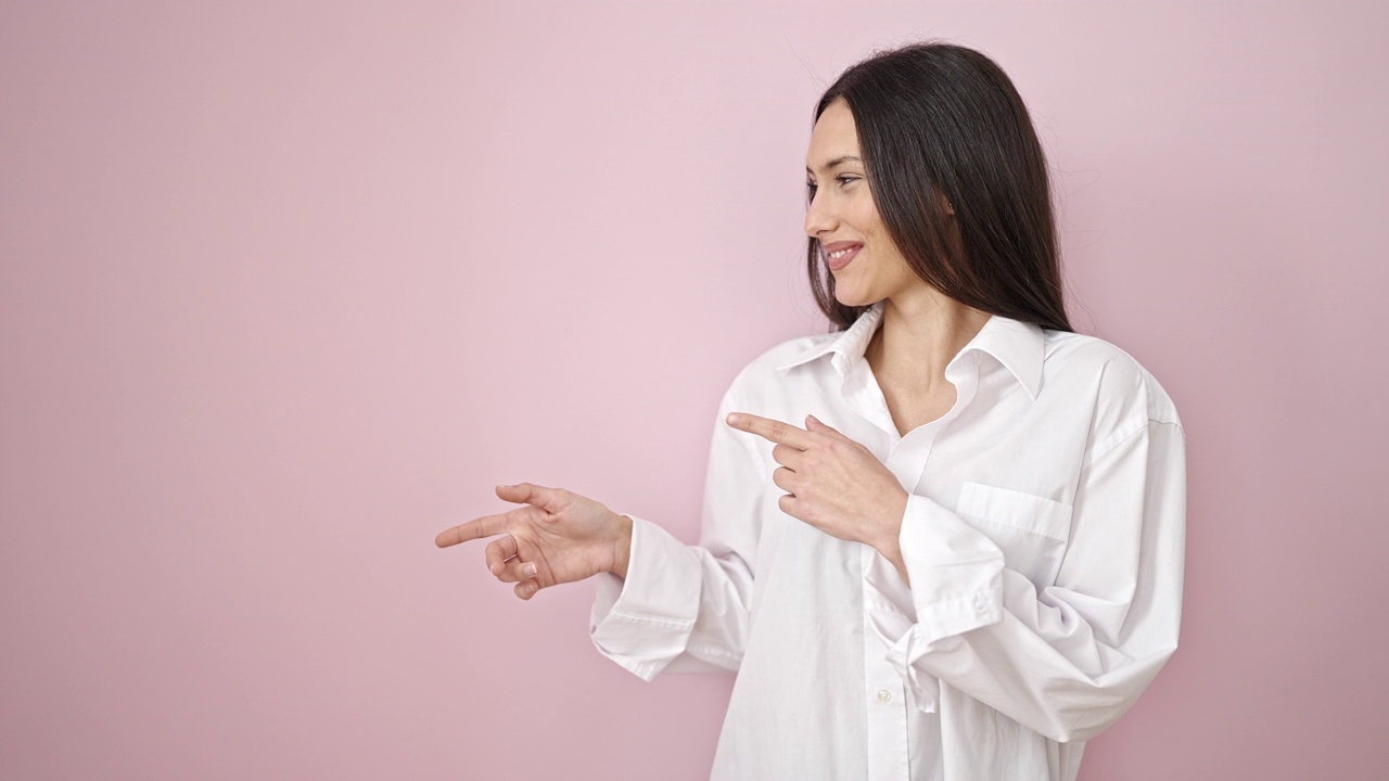 年轻美丽的西班牙女人微笑自信地用手指指着一边孤立的粉红色背景视频素材