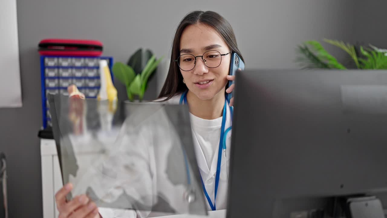 年轻美丽的西班牙女医生拿着x光片在诊所用智能手机说话视频素材