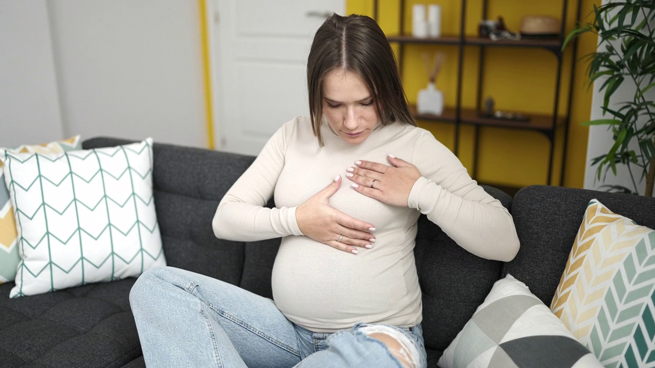 年轻的孕妇坐在家里的沙发上检查乳房视频素材