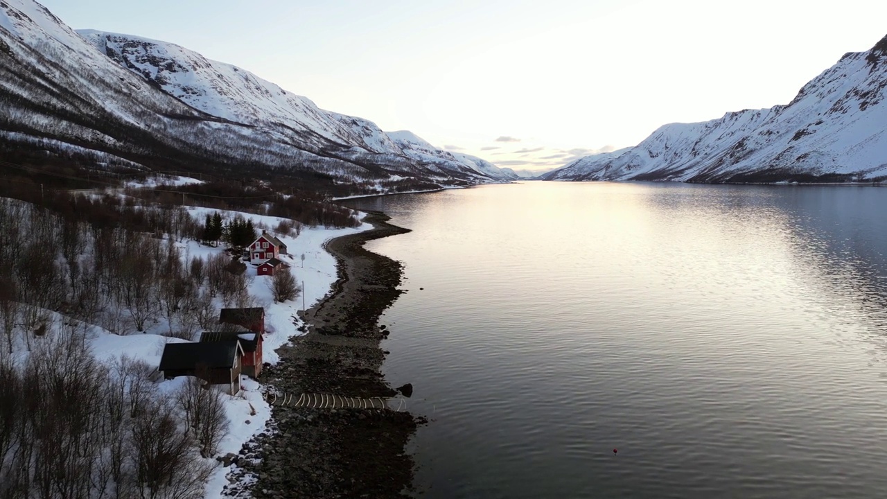 航拍视频显示一条平静的河流，岸边多岩石的雪山上有建筑物视频素材