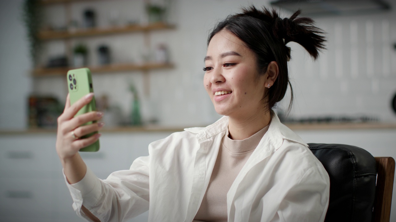 她正在用手机进行视频通话。亚洲女性对着智能手机说话。女性坐在家里上网聊天。视频素材