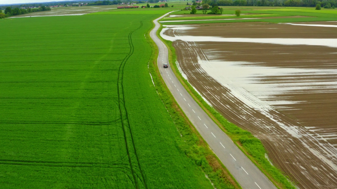 广角鸟瞰被水淹没的农田，一辆黑色汽车沿着道路行驶视频素材