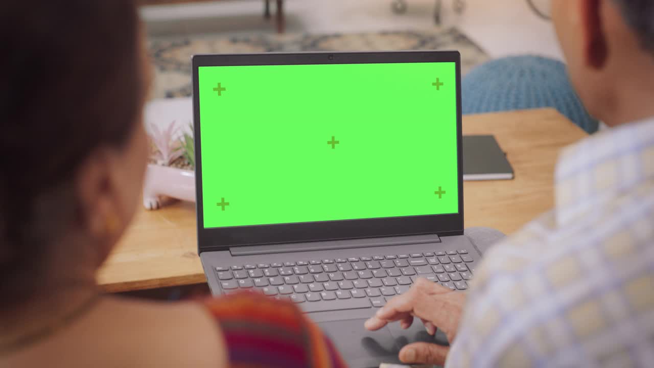 印度老年夫妇使用绿屏笔记本电脑的背影:色度键浏览互联网，在网上购买最好的家居用品，关门，家庭聚会，使用软件，访问网站视频素材