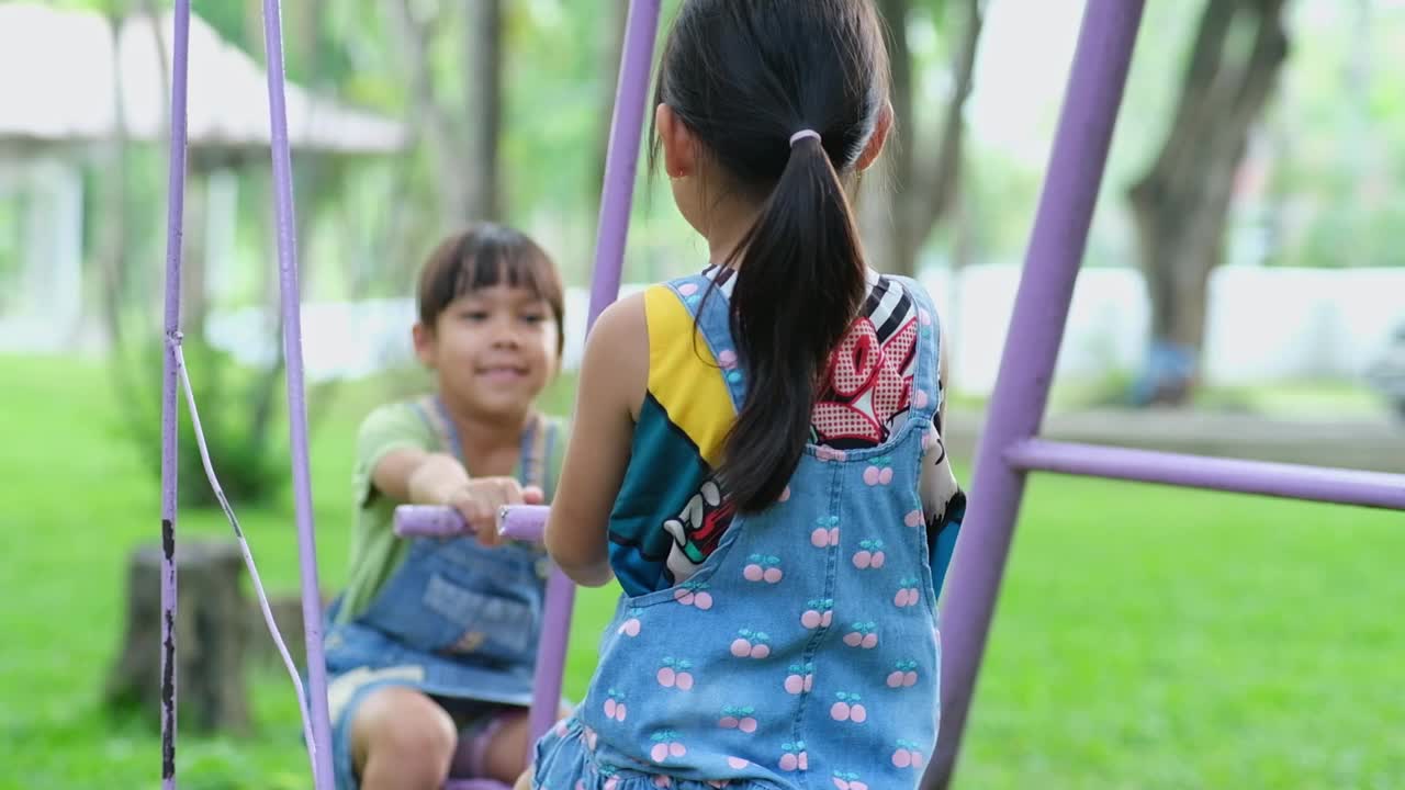 两个可爱的小姐妹在夏天的操场上玩得很开心。可爱的小女孩在操场上笑着摇着马。孩子们的夏季休闲活动。视频素材