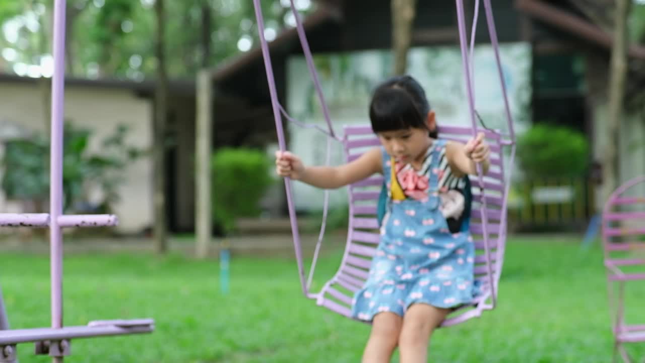 快乐的亚洲女孩在夏天在操场上玩得很开心。可爱的小女孩在操场上荡秋千，带着微笑和笑声。孩子们的夏季休闲活动。视频素材