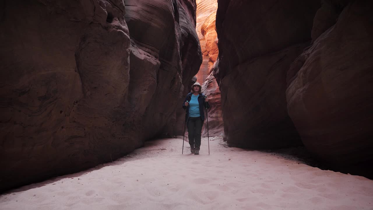 一名妇女在深槽峡谷的干涸河床上徒步旅行，那里有红橙色的弯曲岩石视频素材