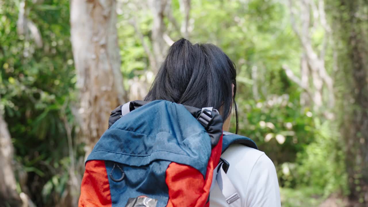 亚洲女徒步旅行者带着背包，微笑着看着镜头，在热带森林中旅行，在大自然中感受新鲜和自由，冒险户外活动人们度假的生活方式。视频素材