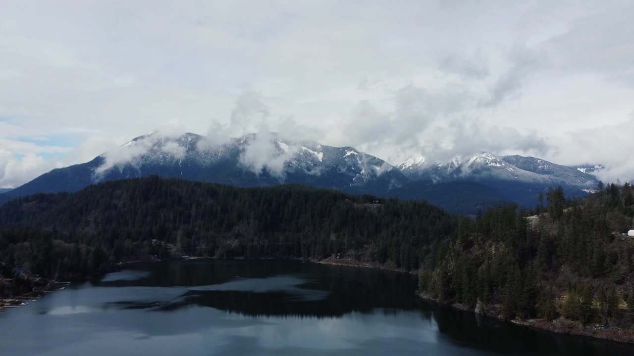 在云雾缭绕的湖泊上空进行空中冒险，周围环绕着雄伟的山脉和林地视频素材