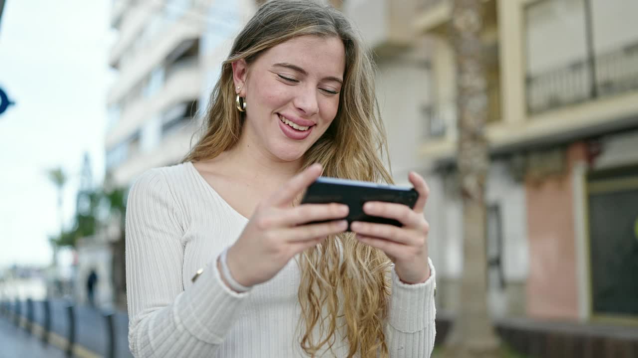 年轻的金发女子微笑着自信地在街上看智能手机视频视频素材