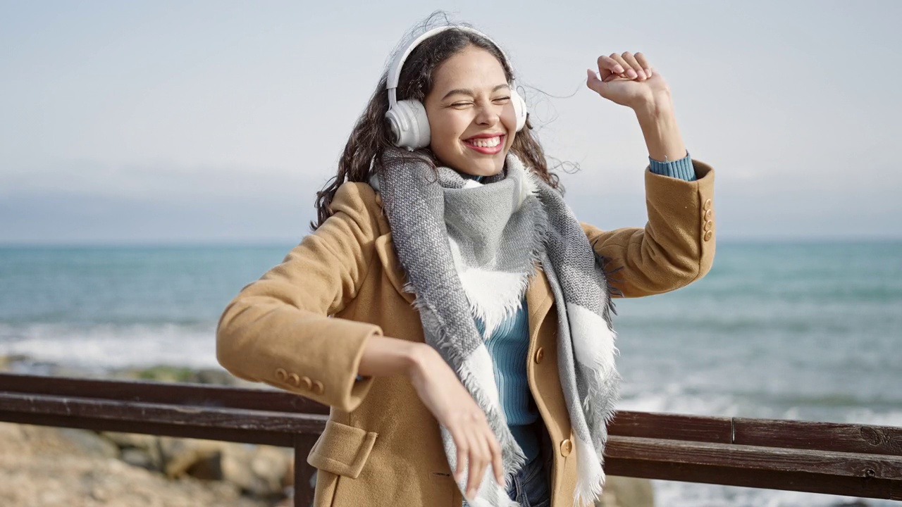 年轻美丽的西班牙女子在海边听音乐跳舞视频素材