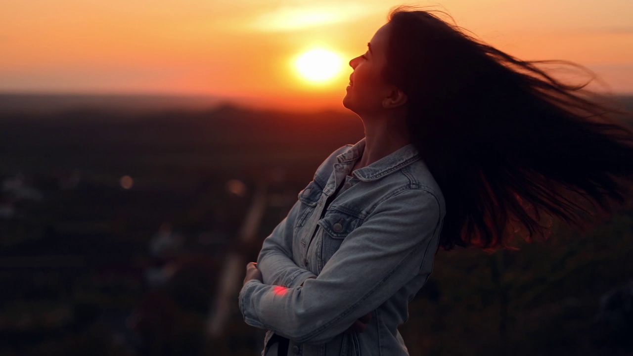 肖像微笑的自然美女高兴地摇着她的头发享受夕阳景观户外。侧视图，慢镜头视频素材