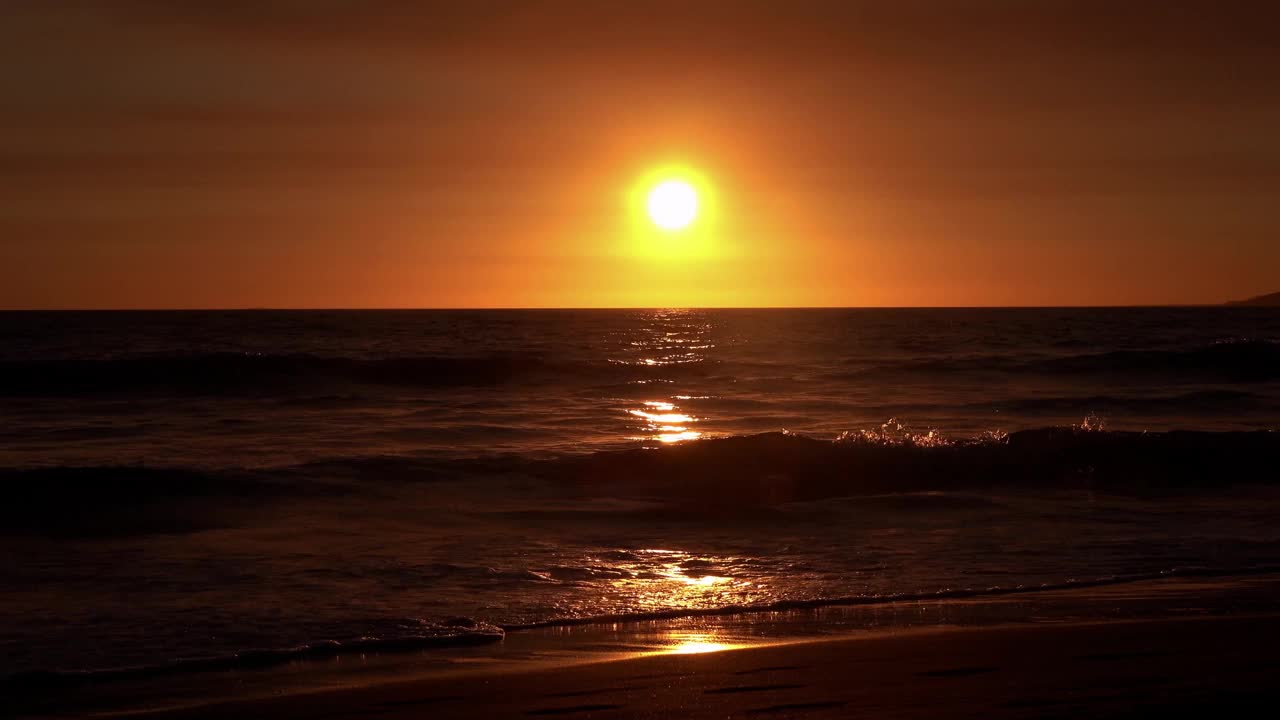 一个人影在海浪中游泳，身后是灿烂的橙色夕阳。视频下载