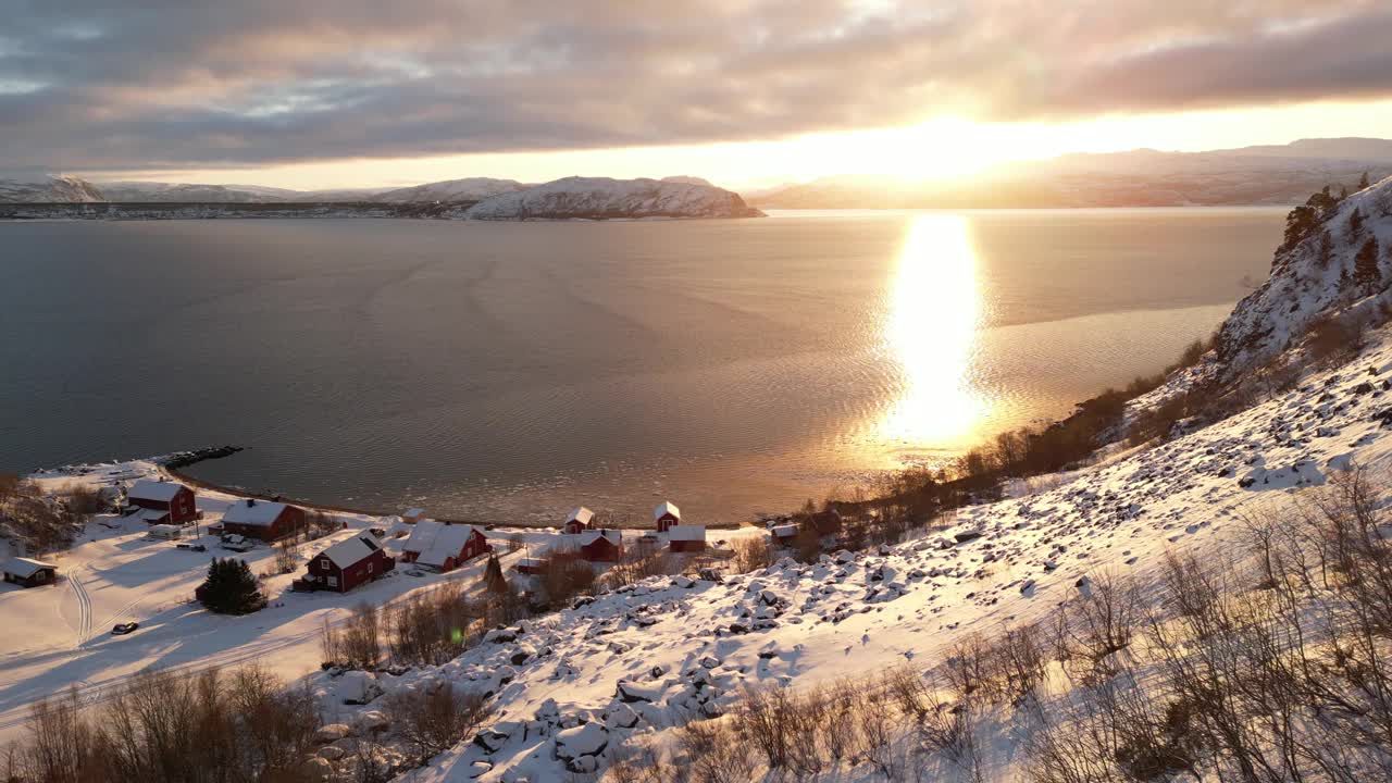 航拍视频显示，日落时，岩石海岸上的建筑物被雪覆盖视频素材