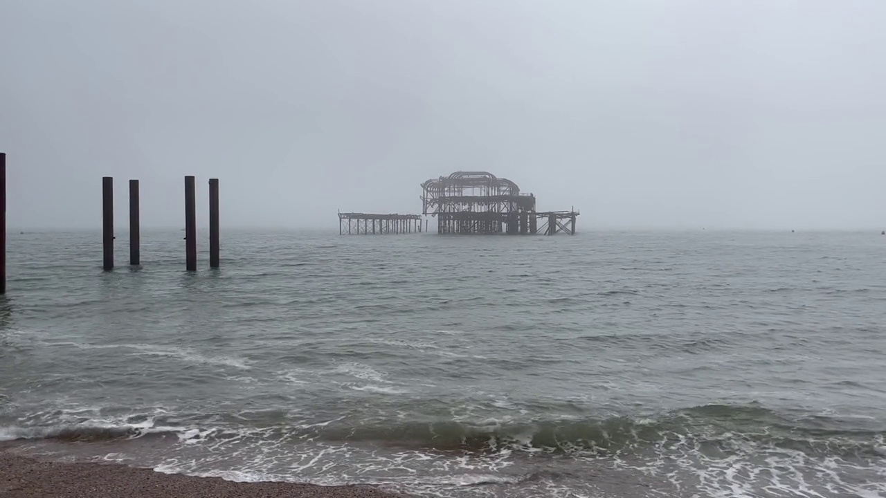 泡沫般的海浪拍打着海岸，背景是一座木制建筑视频素材