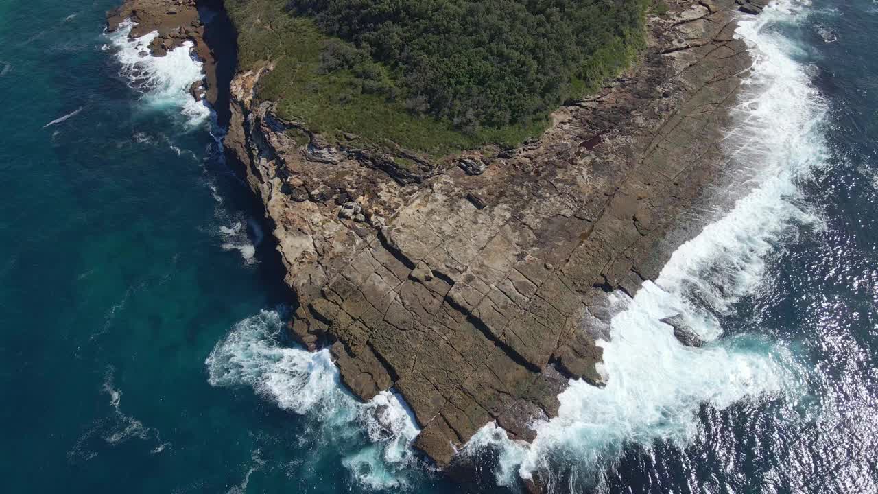 航拍到的泡沫海浪冲击着以绿色森林为背景的岩石岛视频素材