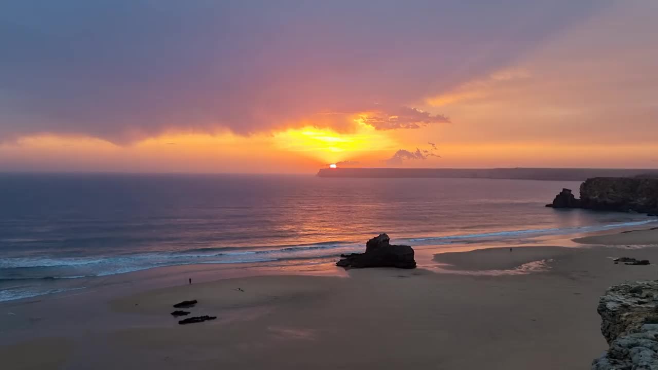 美丽的海景，神奇的沙滩上有石头，地平线上有橙色多云的天空视频素材