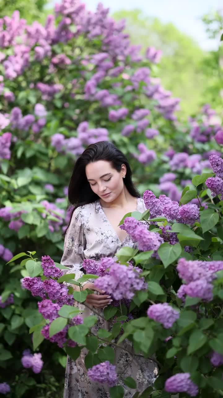 年轻漂亮的女人喜欢在花园里盛开的丁香灌木。视频下载