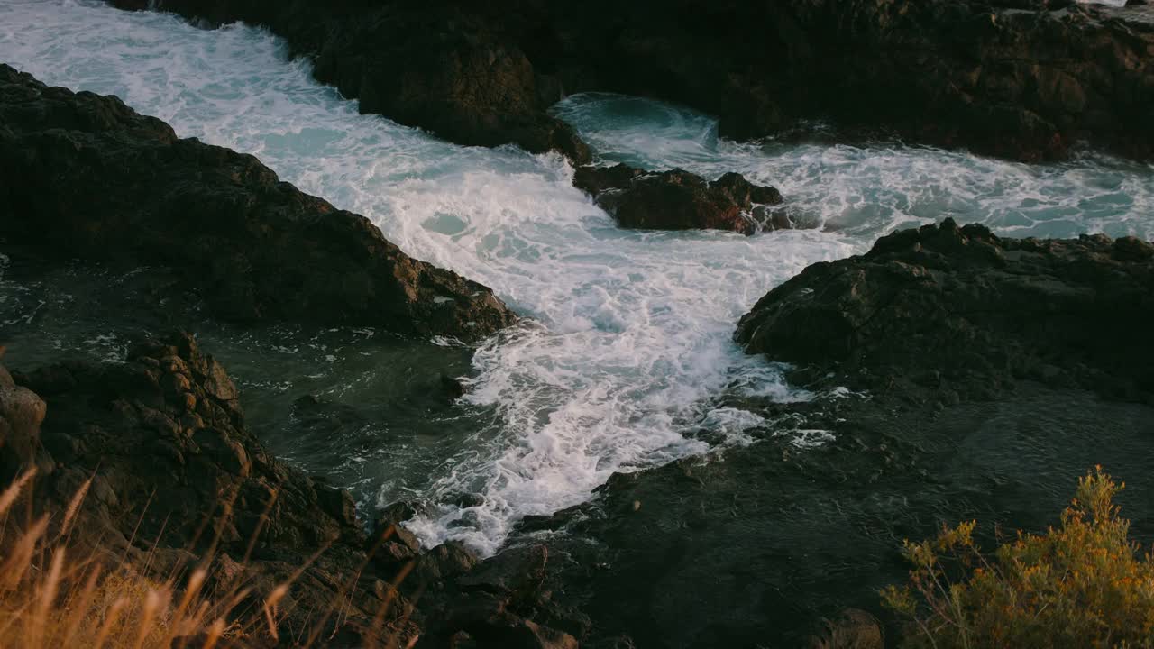 在金色的夕阳下，海浪拍打着岩石海滩。特写:狂暴的暴风雨泡沫，水溅在火山岸边。视频素材