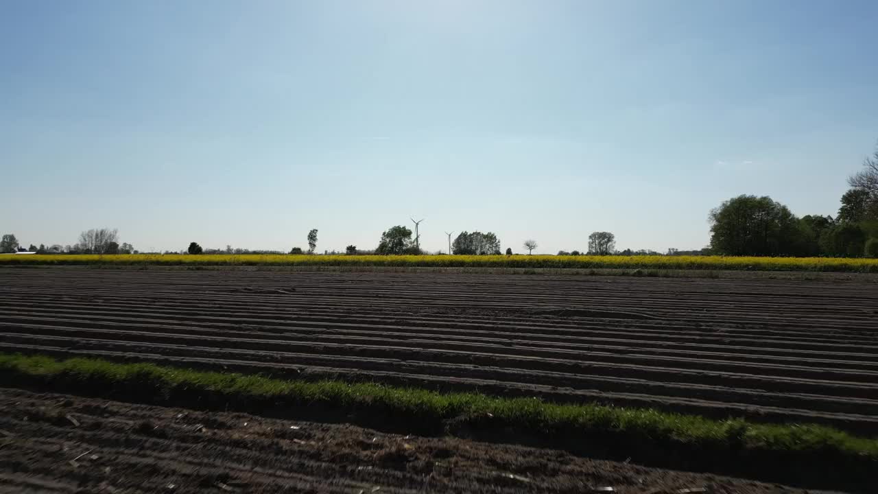 在一个阳光明媚的日子里，无人机在有树木和风车的耕地和草地上低空飞行视频素材