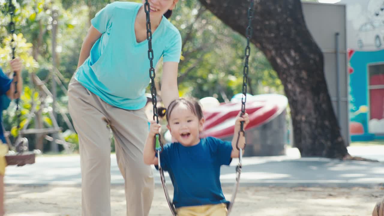 母亲和孩子们在操场秋千上嬉戏视频素材