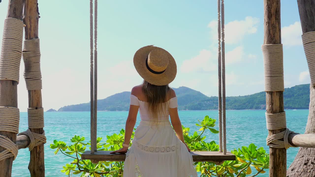 夏季旅游概念。戴草帽的女子荡秋千，欣赏海景视频素材