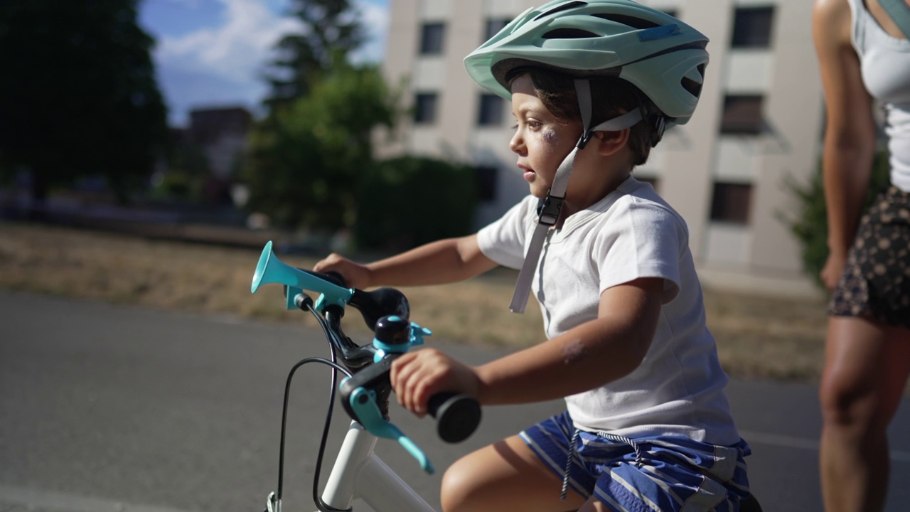 孩子带着头盔跟着妈妈在外面学骑自行车。父母教小男孩骑自行车。儿童发展视频素材