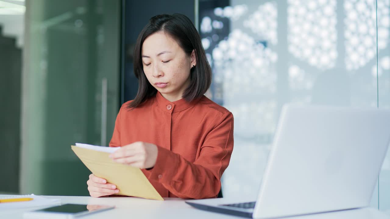 悲伤的亚洲妇女坐在现代办公室的工作场所读着带坏消息的信视频素材