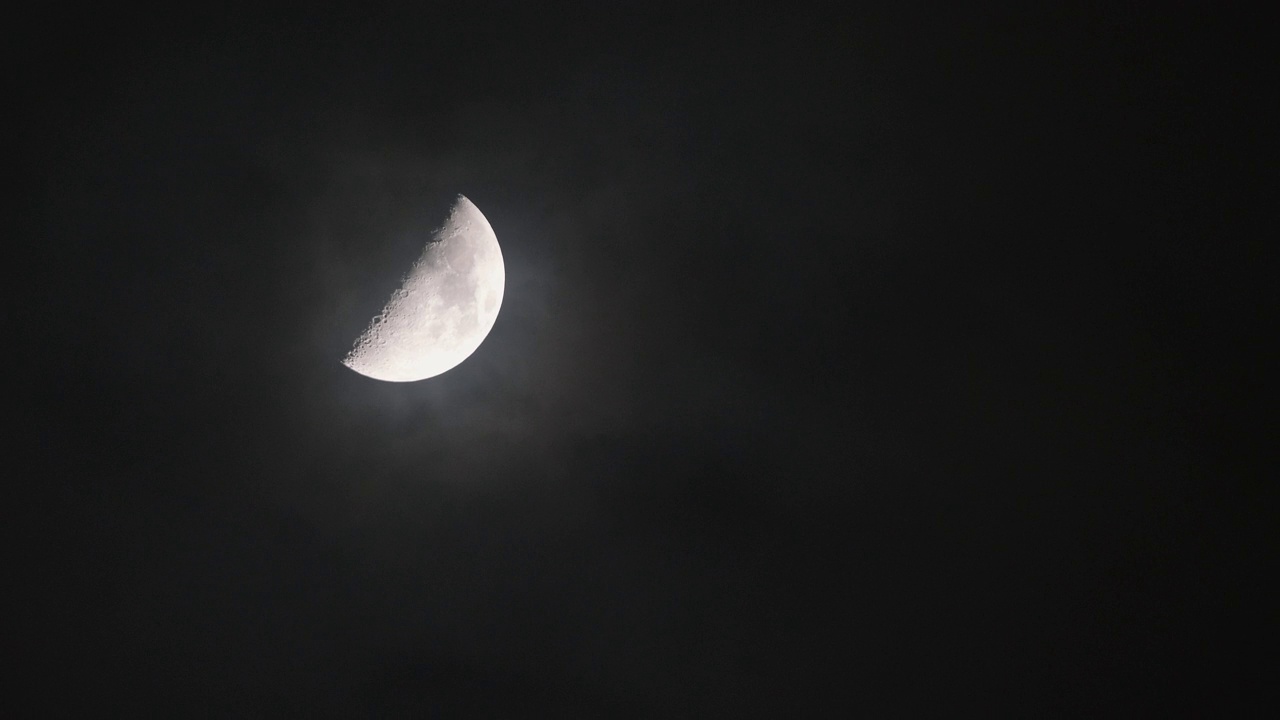 近景半月，夜间黑色天空背景，云彩移动，月光闪耀，长焦镜头4k慢动作镜头。视频素材