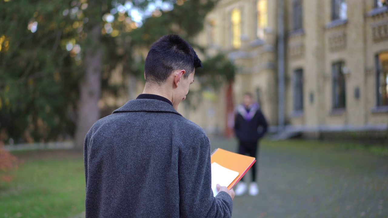 后景年轻的白人男子慢镜头漫步在大学校园，非洲裔美国学生路过离开。跟踪拍摄自信聪明的家伙走向大学。视频素材