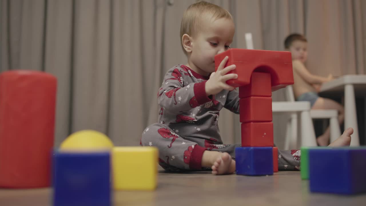 toddler baby sits wooden floor gray pajamas plays multi-colored plastic cubes视频素材