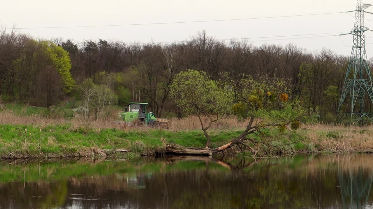 拖拉机沿着森林里的河岸或湖岸行驶视频下载