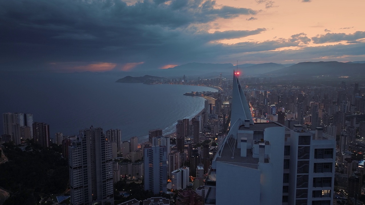 临海的现代化城市，夜晚紧挨着深蓝色的海洋。橙色的夕阳和黑暗的乌云在背景中。视频素材