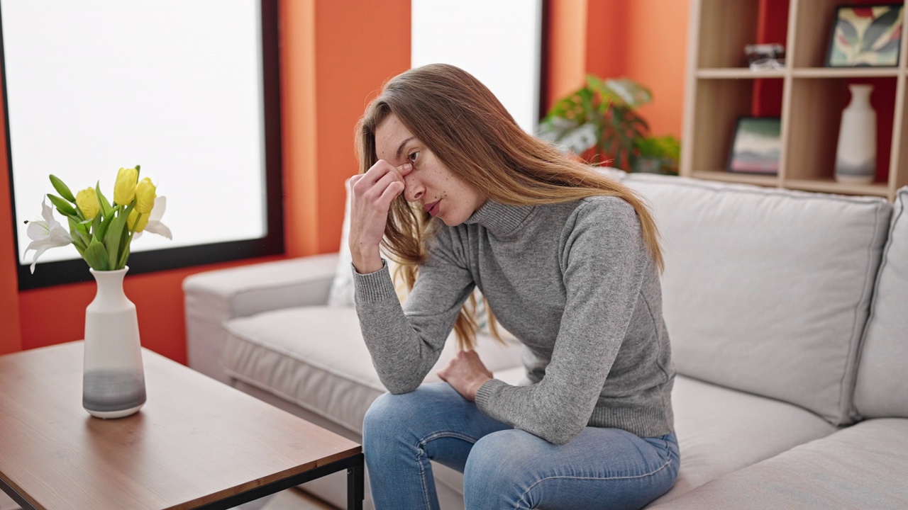 年轻的白人妇女坐在家里的沙发上，表情严肃视频素材