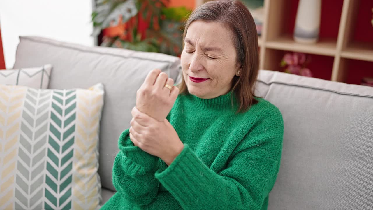 白发苍苍的成熟西班牙女人坐在家里的沙发上忍受手腕疼痛视频素材