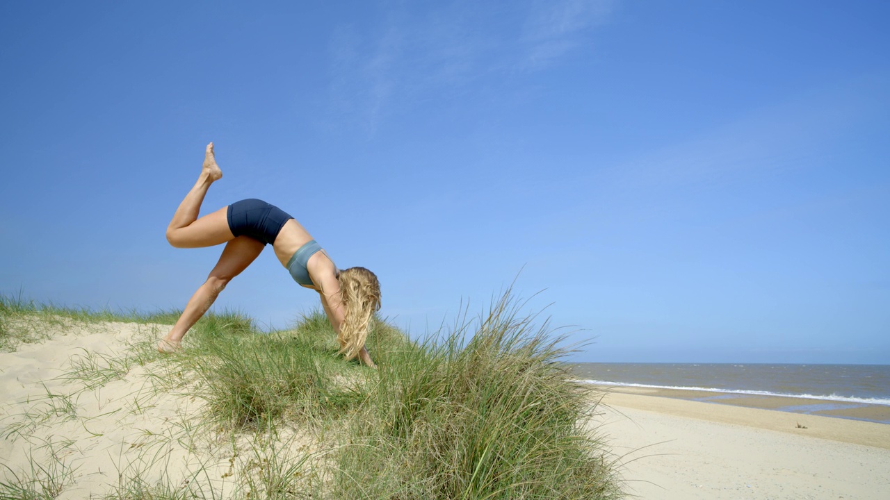 A woman practising Yoga on a sunny beach.视频素材