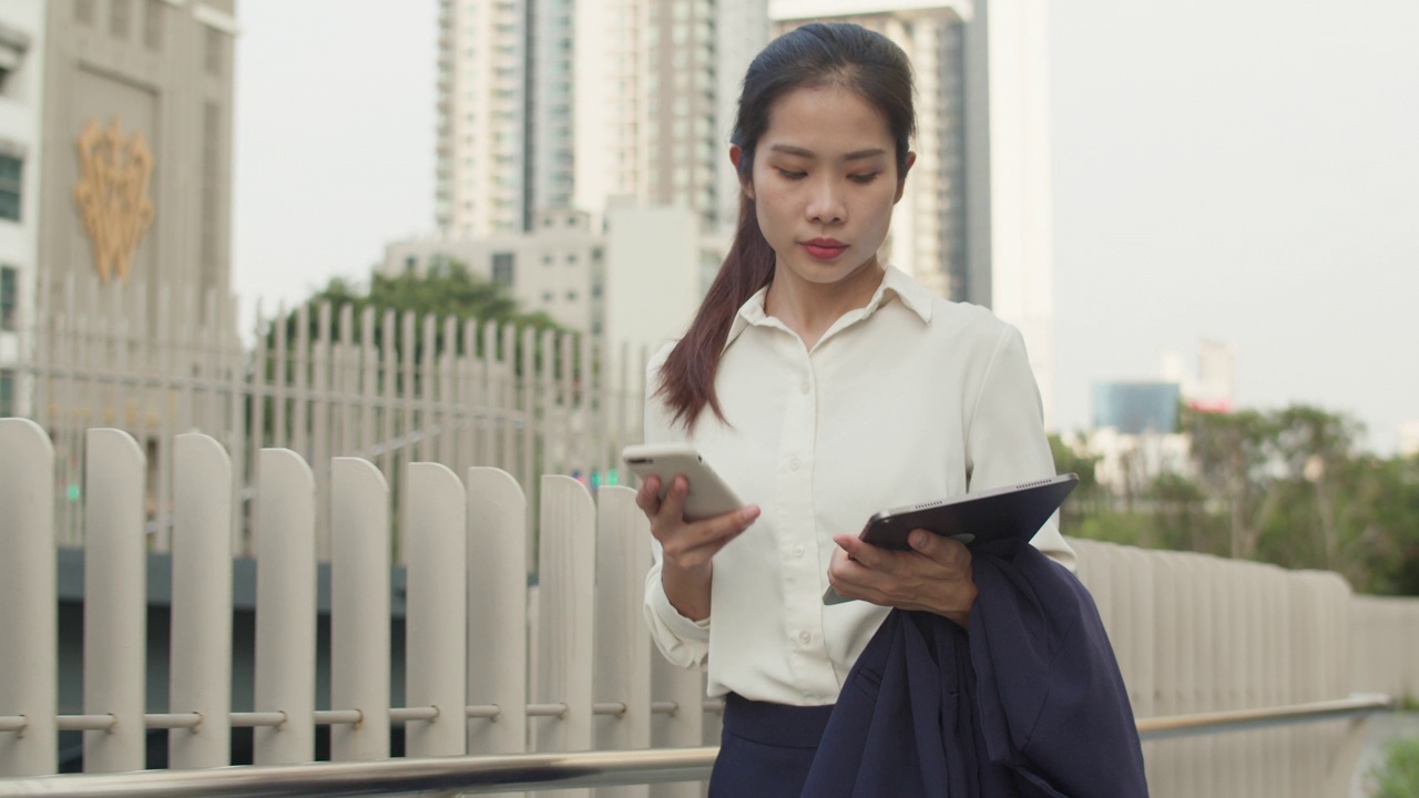 自信的女商人拿着智能手机，发短信，走在城市街道上上网。视频素材