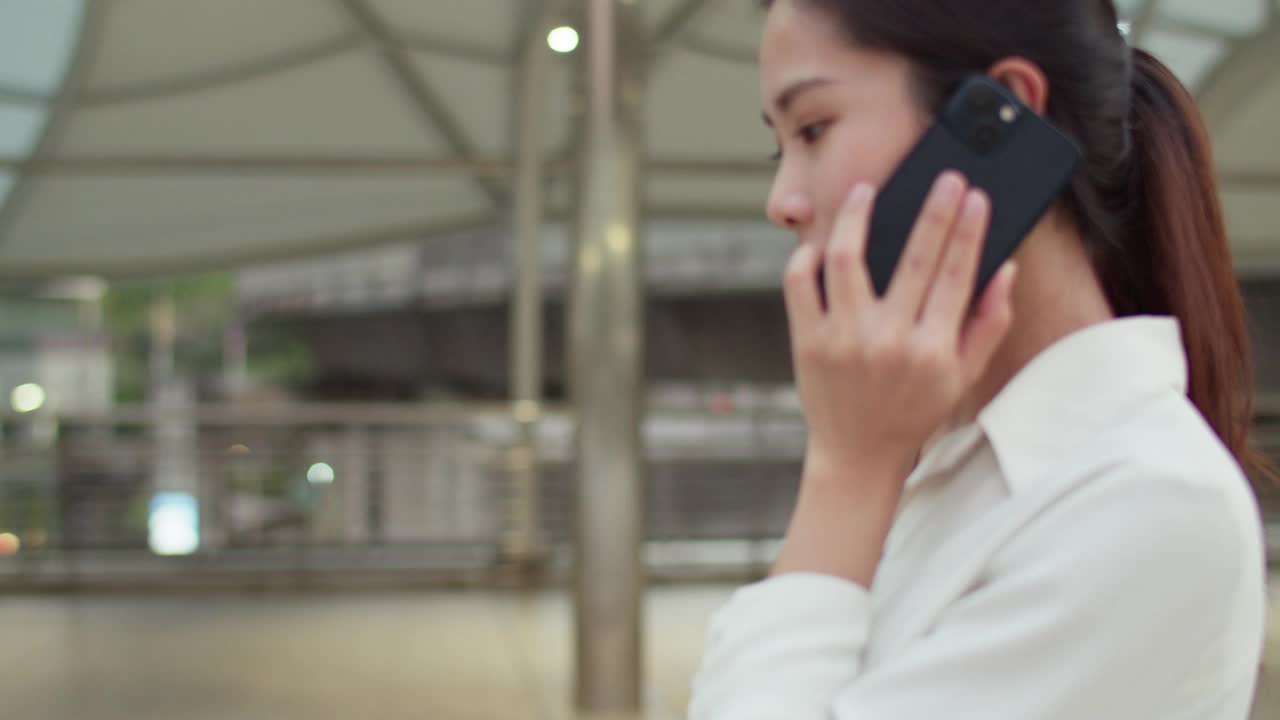 年轻漂亮的亚洲女商人在城市的街道上边走边讲手机。视频素材