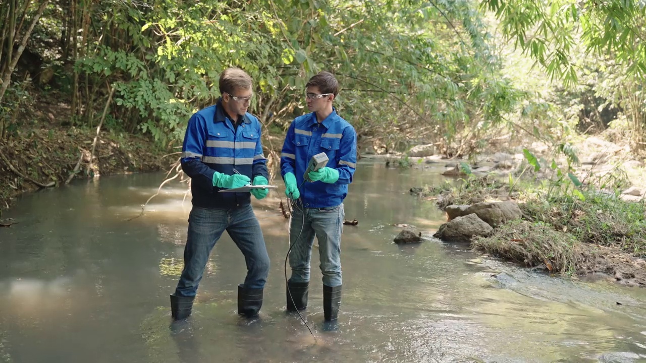 两名男性生物学家在当地的一条河里测试水。生态学家们穿着休闲服，在湖上探险，取水样。视频下载